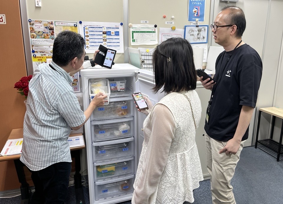 冷凍庫からタベレルの商品を選び、スマートフォンで購入する社員